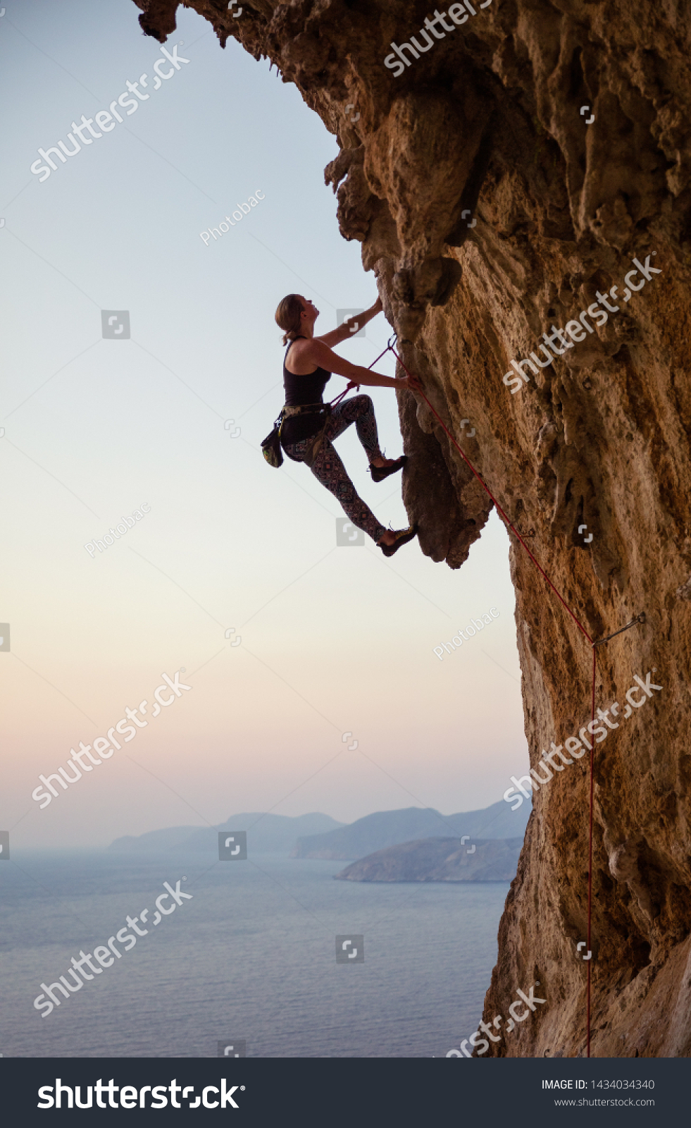 Young woman climbing challenging route at sunset #1434034340