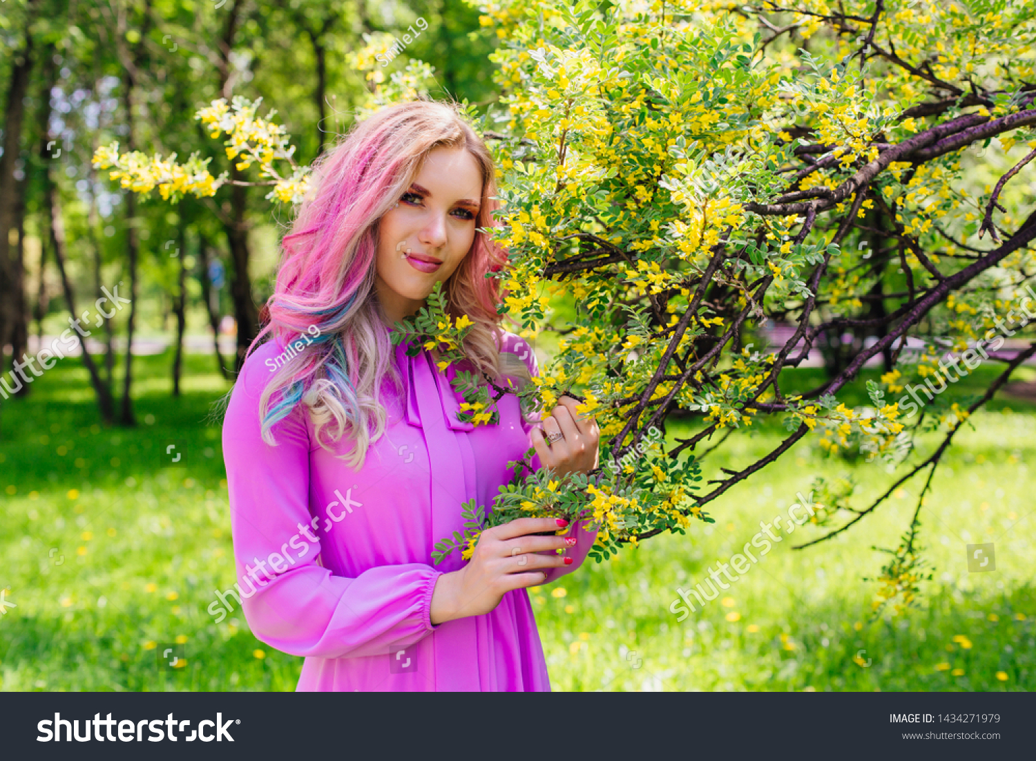 Beautiful fashion model girl with colorful dyed hair and perfect makeup and hairstyle standig next to blooming barberry bush with yellow flowers #1434271979