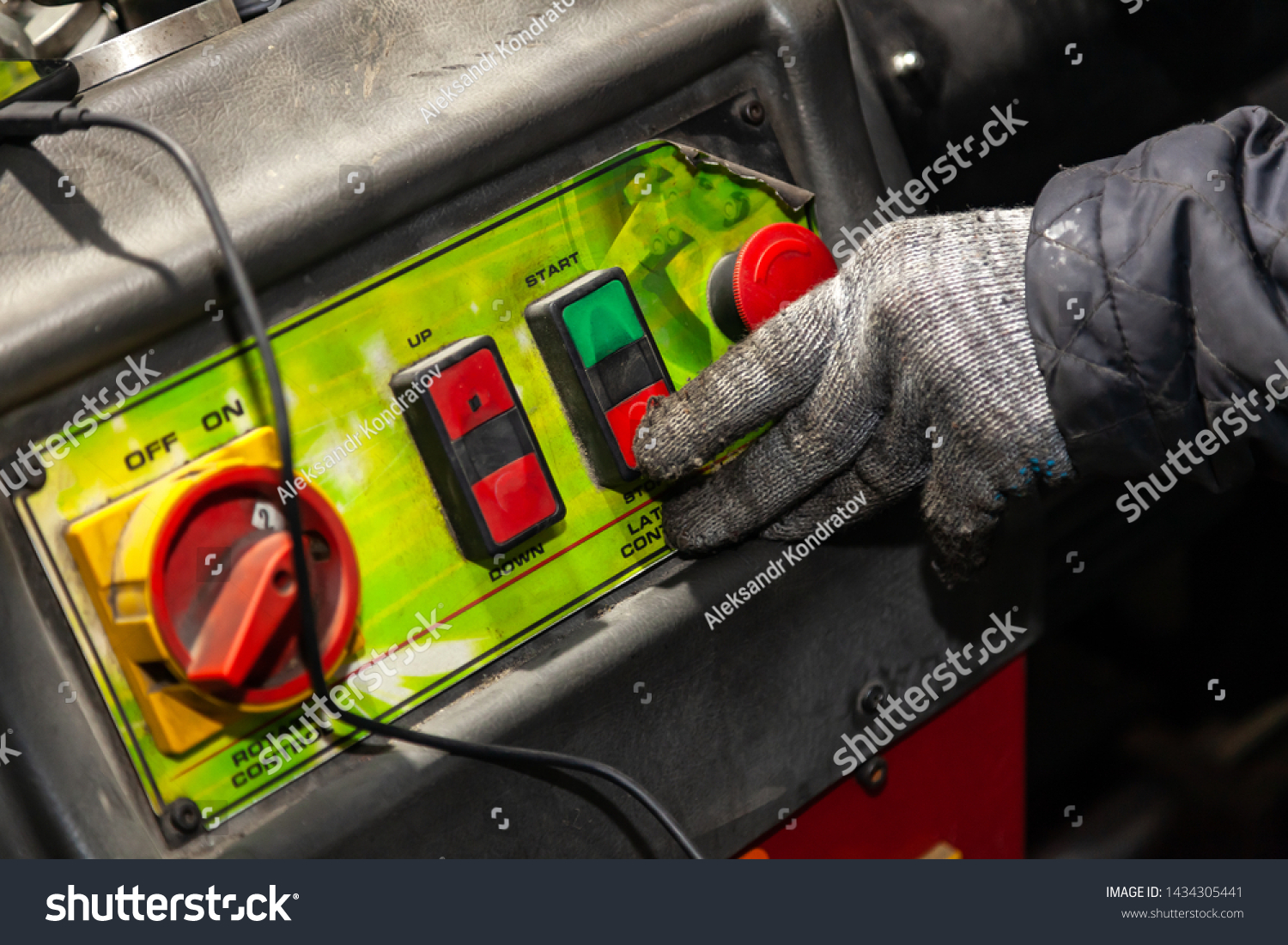 A male worker in working gloves presses the red button on the machine control panel in a workshop or factory. Industry and production in engineering. #1434305441