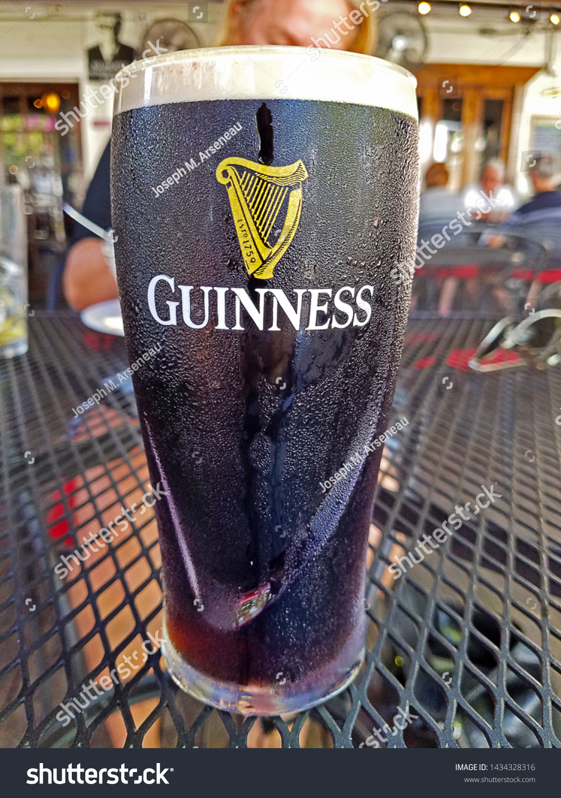 TAMPA, FLORIDA - FEBRUARY 22, 2019: A pint of Guinness presented on an outdoor mesh table. Rich and creamy. Distinctively black. Velvety in its finish. This iconic beer is defined by harmony. #1434328316