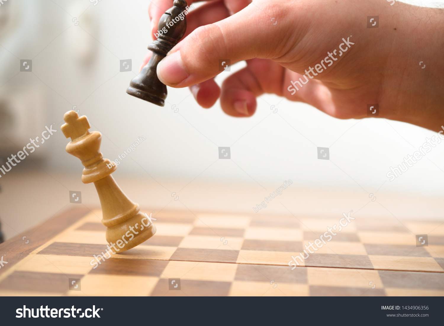Hand holding a black bishop while it's hitting the white king in a check mate, chess game. #1434906356