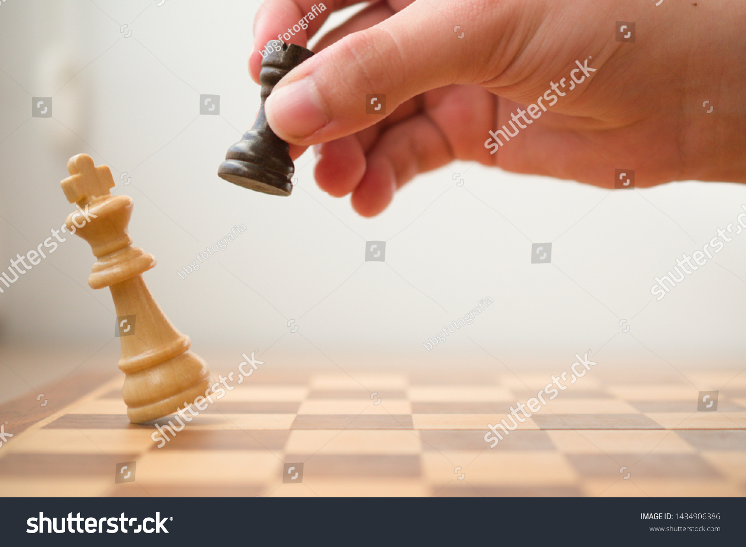 Hand holding a black tower while it's hitting the white king in a check mate, chess game. #1434906386