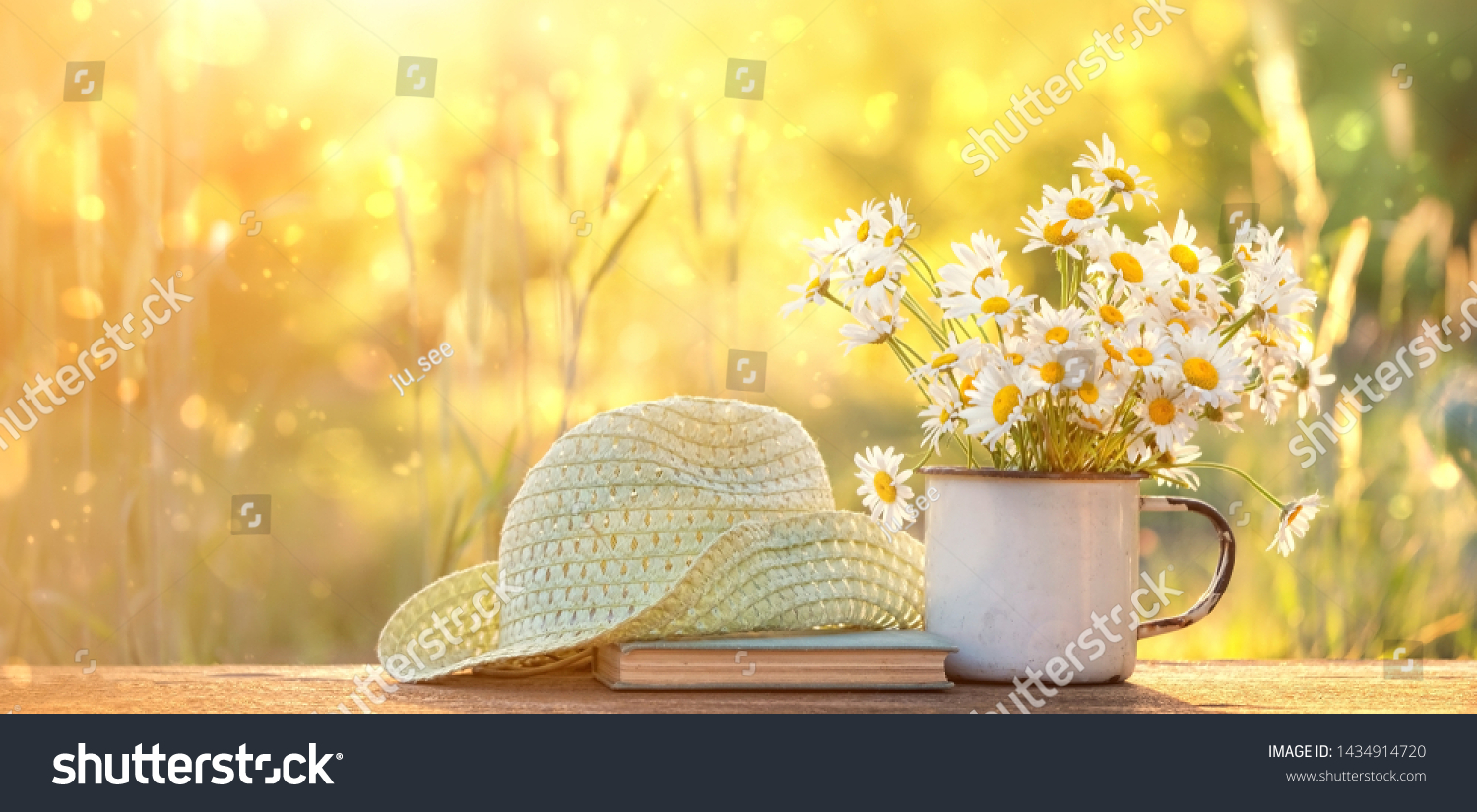 summer nature background. chamomile flowers in white mug, book, braided hat on table in garden. summer season. rustic composition with flowers. relax time. copy space #1434914720