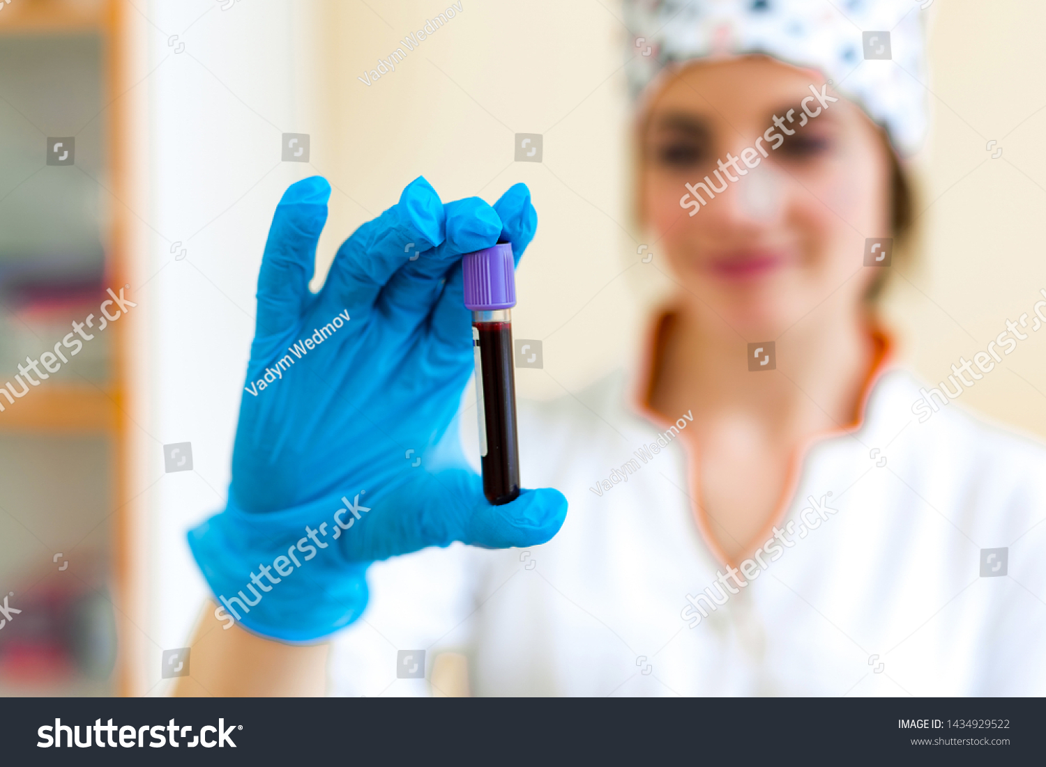 Test tube with blood in the hand of a laboratory technician. Female specialist is holding a vial of red liquid with sterile blue glove indoors. Close-up. #1434929522