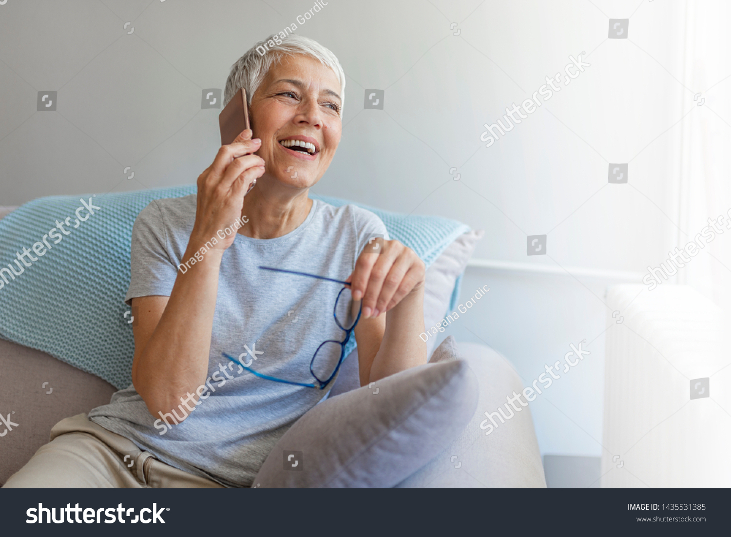 Senior woman talking on her mobile phone. Senior woman has a happy conversation at cellphone. Smiling senior woman using phone sitting on couch at home. #1435531385