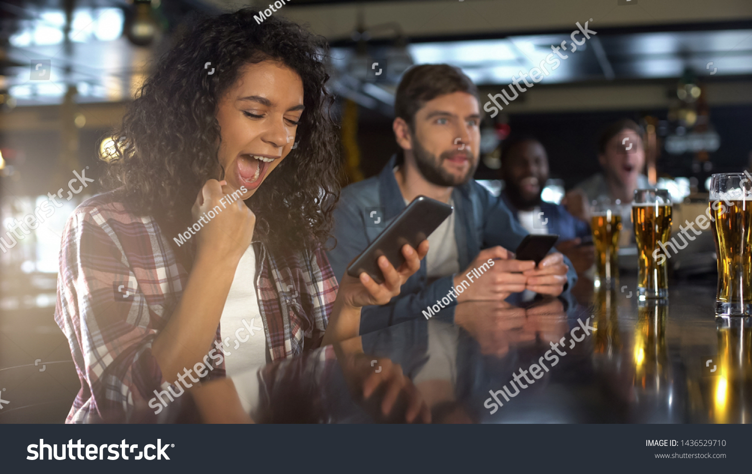 Cheerful biracial lady in pub celebrating successful bet on sports, online app #1436529710