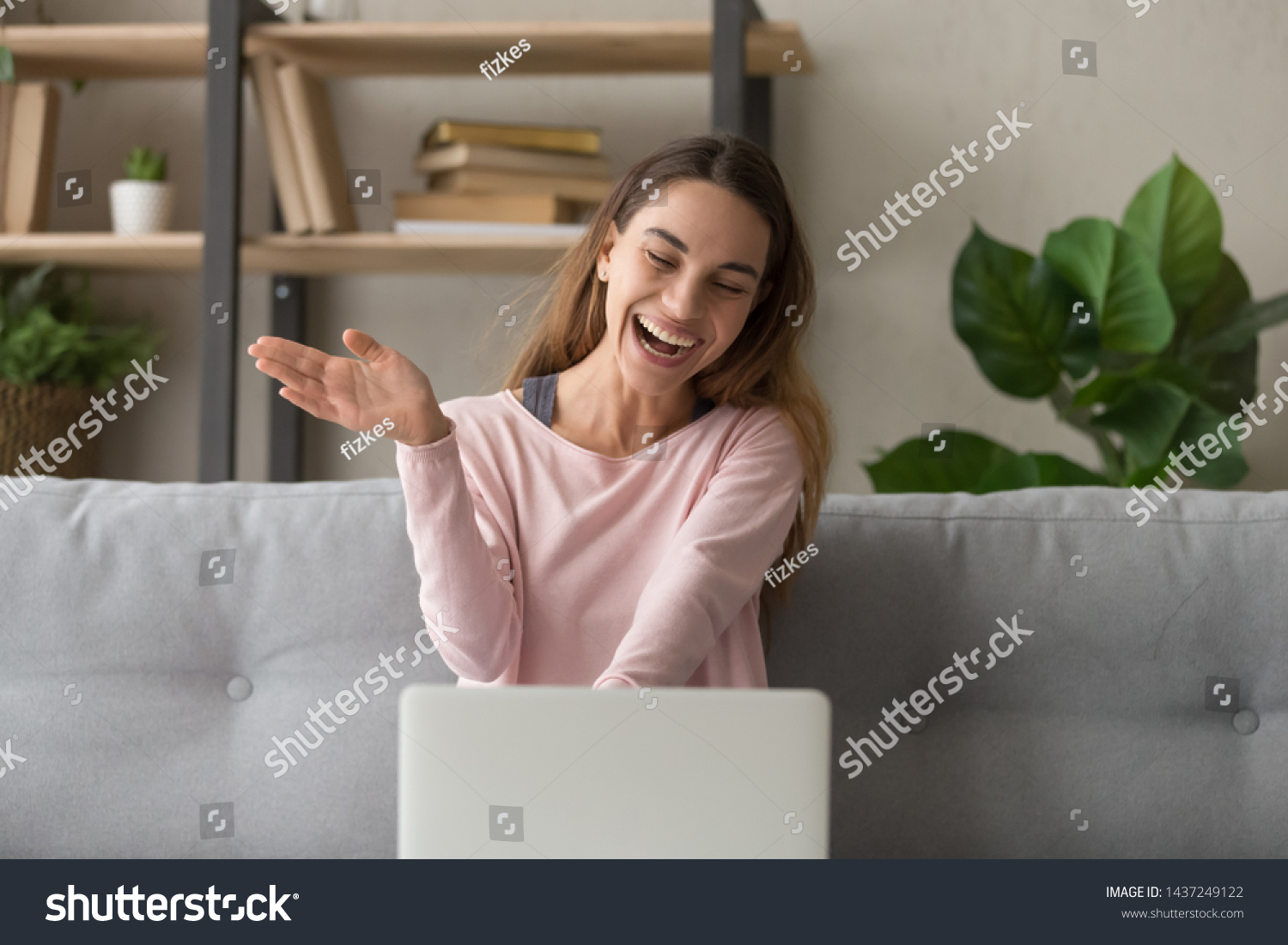 Smiling girl sit on couch at home wave talk with friend or family having video call on laptop, happy young woman greeting say hello, speak communicate using dating online application on computer #1437249122