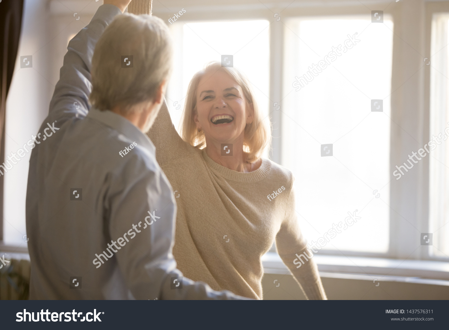 Happy middle aged mature woman enjoying dancing with elder husband at home, active healthy senior old couple man and woman pensioners having fun in waltz laughing bonding celebrating anniversary #1437576311