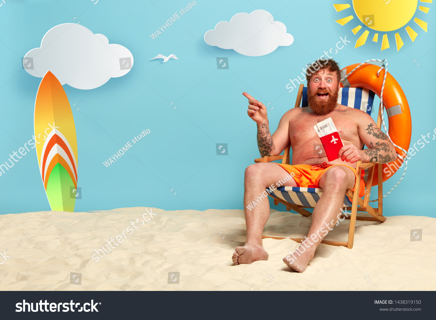 Topless happy redhaired guy shows passport with tickets, points on free space, poses at beach on comfortable chair, likes surfboarding, enjoys tropical resort. Traveling and vacation concept #1438319150