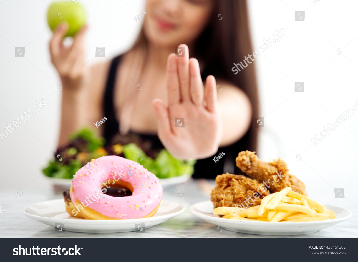 Young girl on dieting for good health concept. Close up female using hand reject junk food by pushing out her favorite sweet donuts and fried chicken and choose green apple and salad for good health. #1438461302