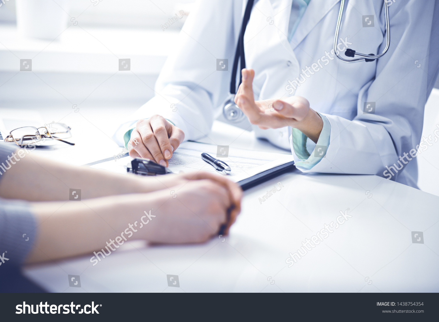 Doctor and female patient sitting at the desk and talking in clinic near window. Medicine and health care concept. Green is main color #1438754354