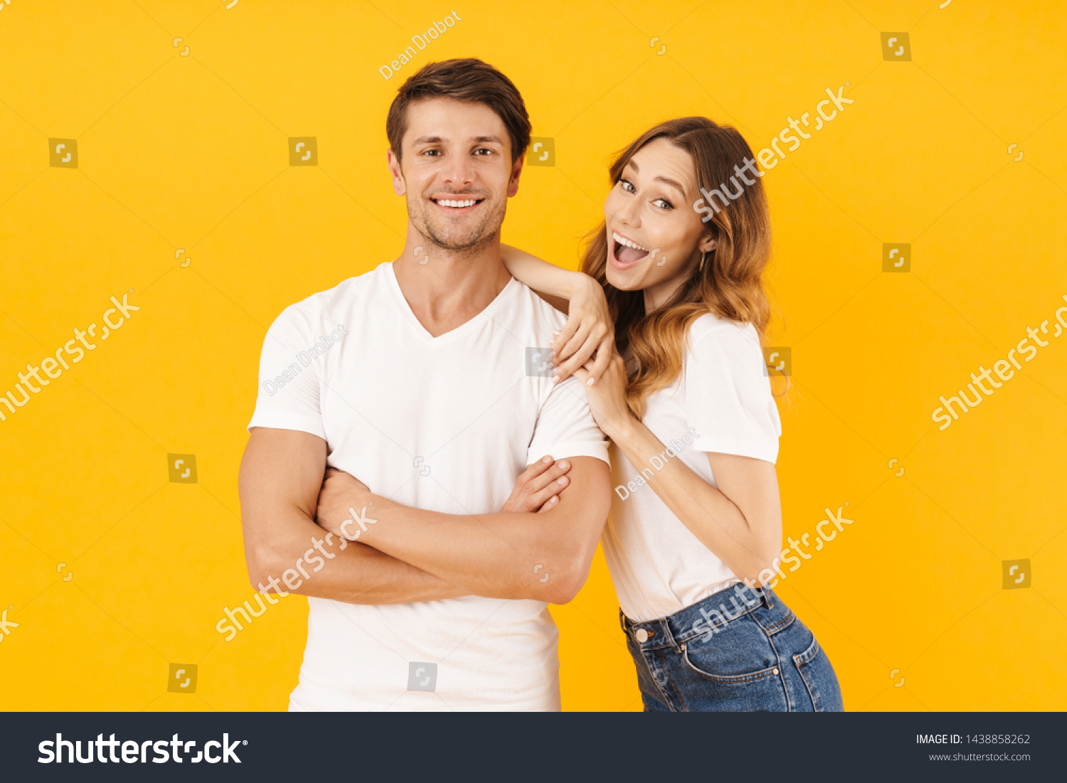 Portrait of joyous couple man and woman in basic t-shirts smiling and hugging together isolated over yellow background #1438858262