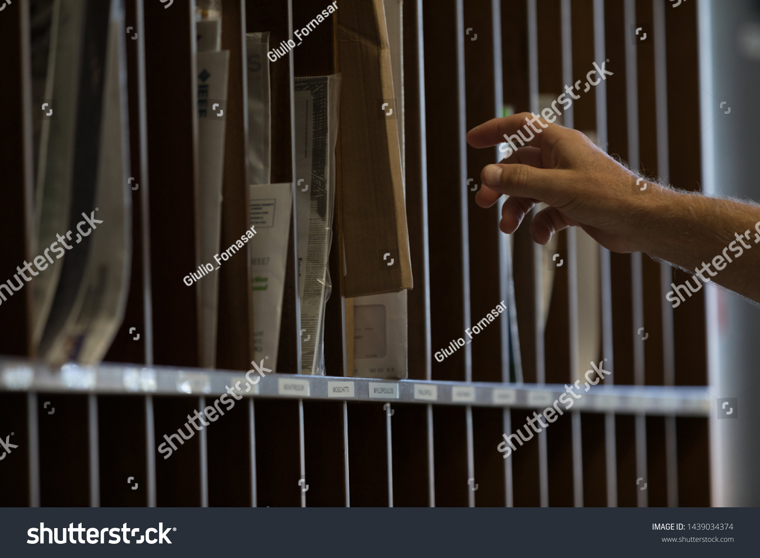 Male hand reaching for sorted post or mail in pigeon holes in a postal depot in a corporate business #1439034374