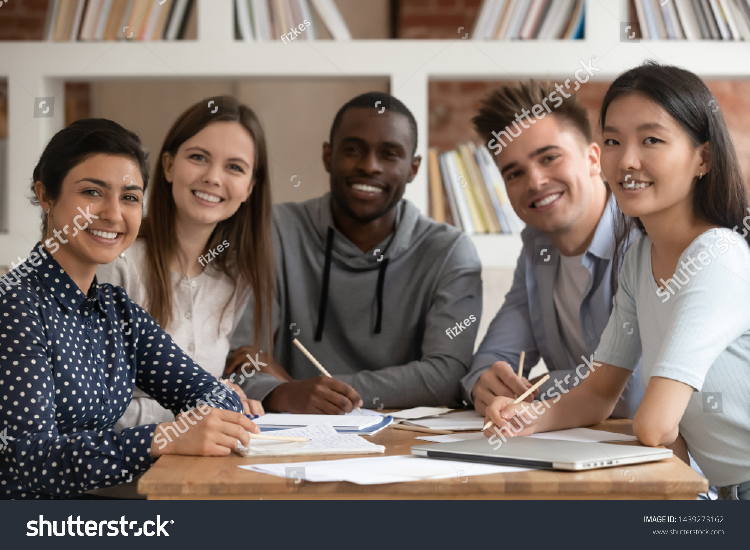 Group picture of happy multiethnic young people sit at shared desk look at camera studying together, multicultural excited students or groupmates smiling posing for photo working in library #1439273162