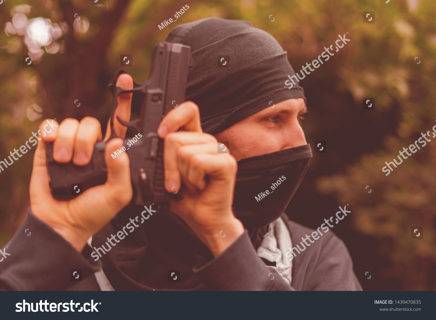 burglar in mask holding and reloading the pistol outdoor #1439470835