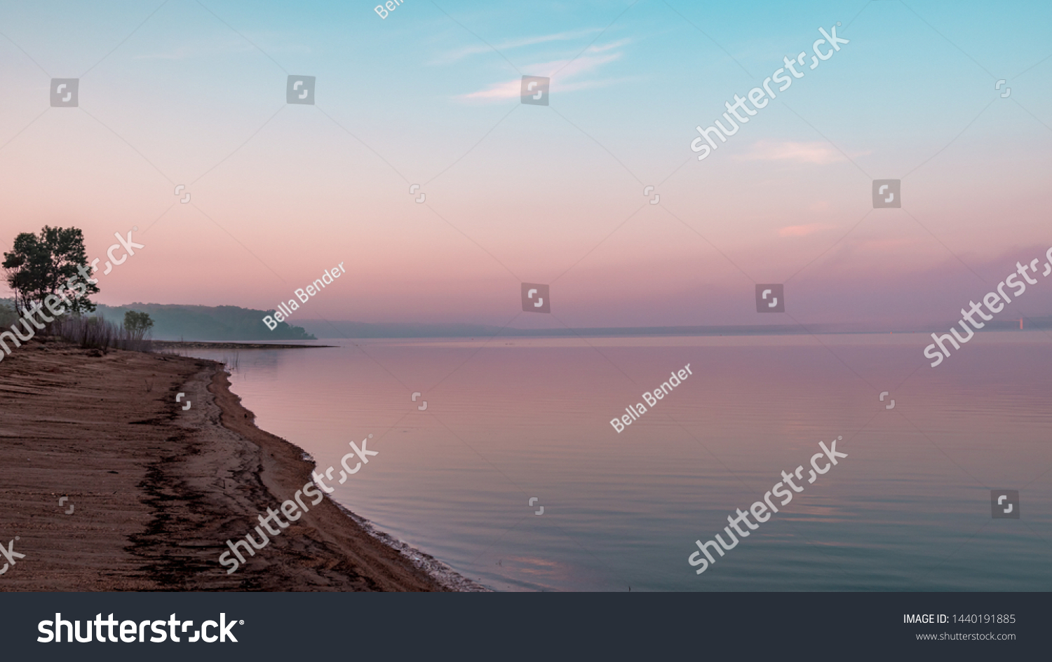 Shoreline and reflection of pink clouds on a lake. Saylorville Lake, near Polk City, Iowa, USA. Blue hour, fog in the distance, cotton candy clouds, sunrise in the Midwest.  #1440191885