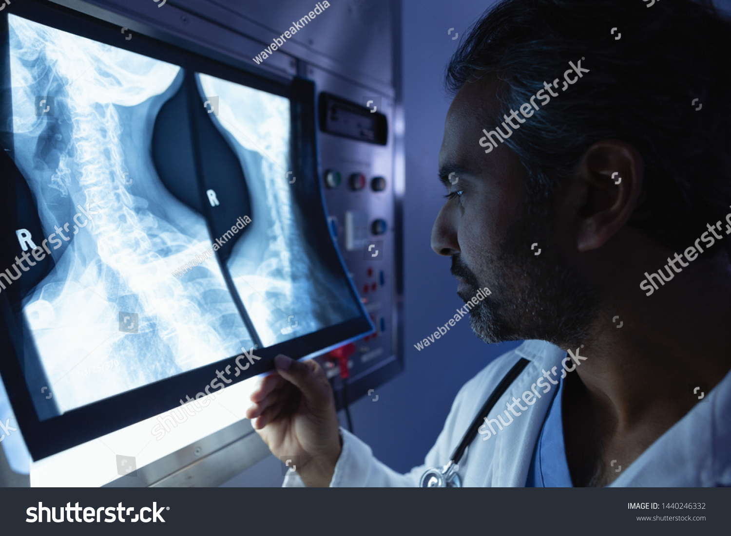 Side view of mature mixed race male doctor examining x-ray on x-ray light box in operation room at hospital #1440246332