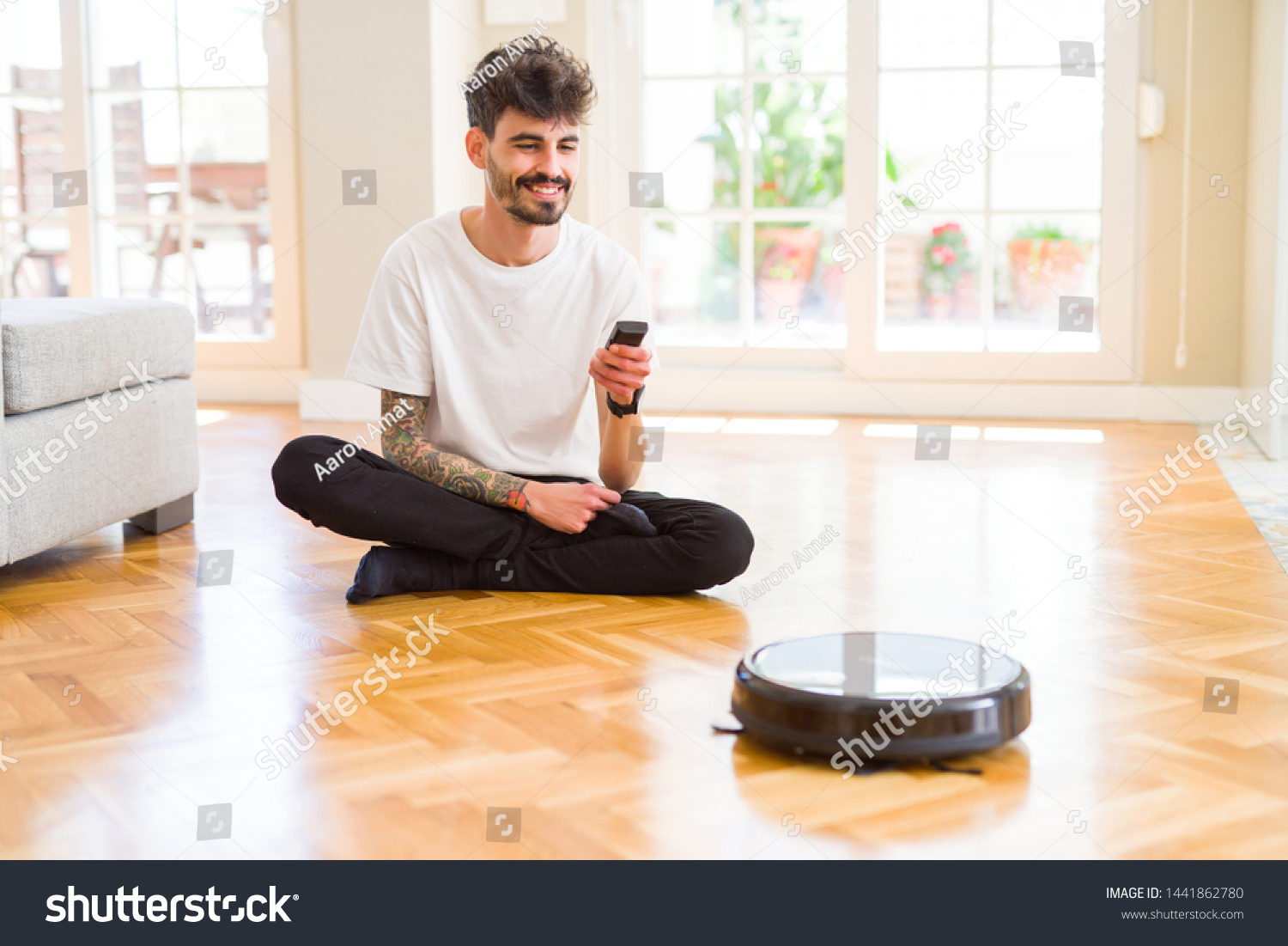 Young man using automatic vacuum cleaner to clean the floor, controling machine housework robot #1441862780