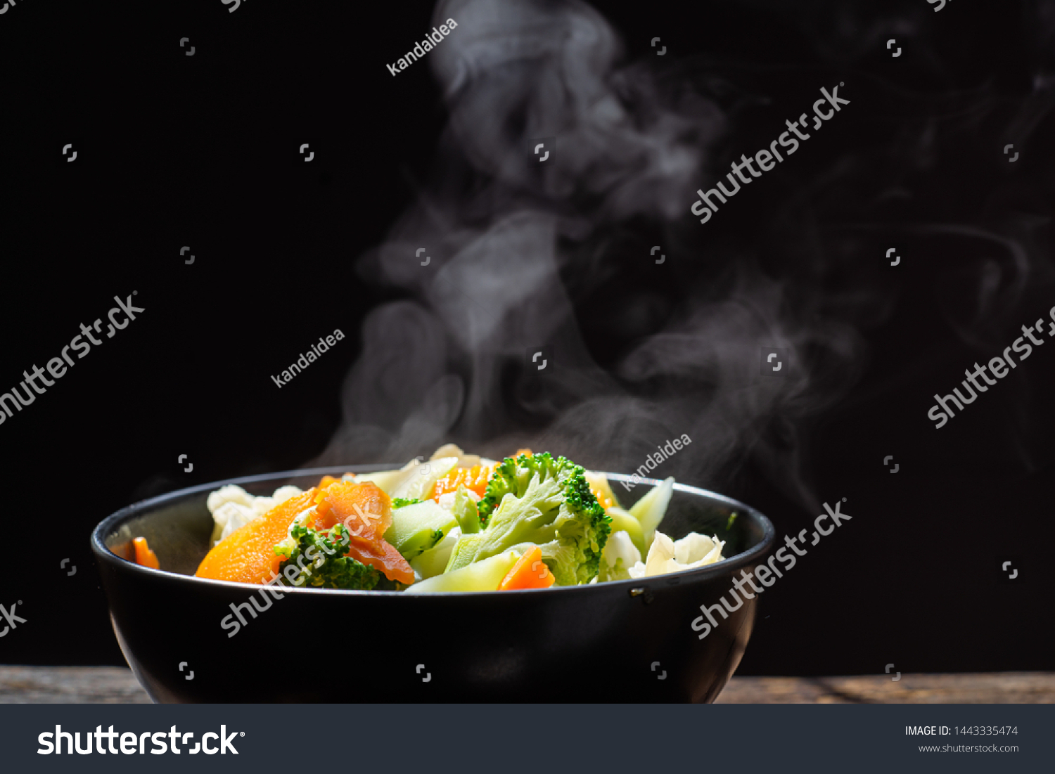 The steam from the vegetables carrot broccoli Cauliflower in black bowl  , a steaming. Boiled hot Healthy food on table on black background,hot food and healthy meal concept #1443335474