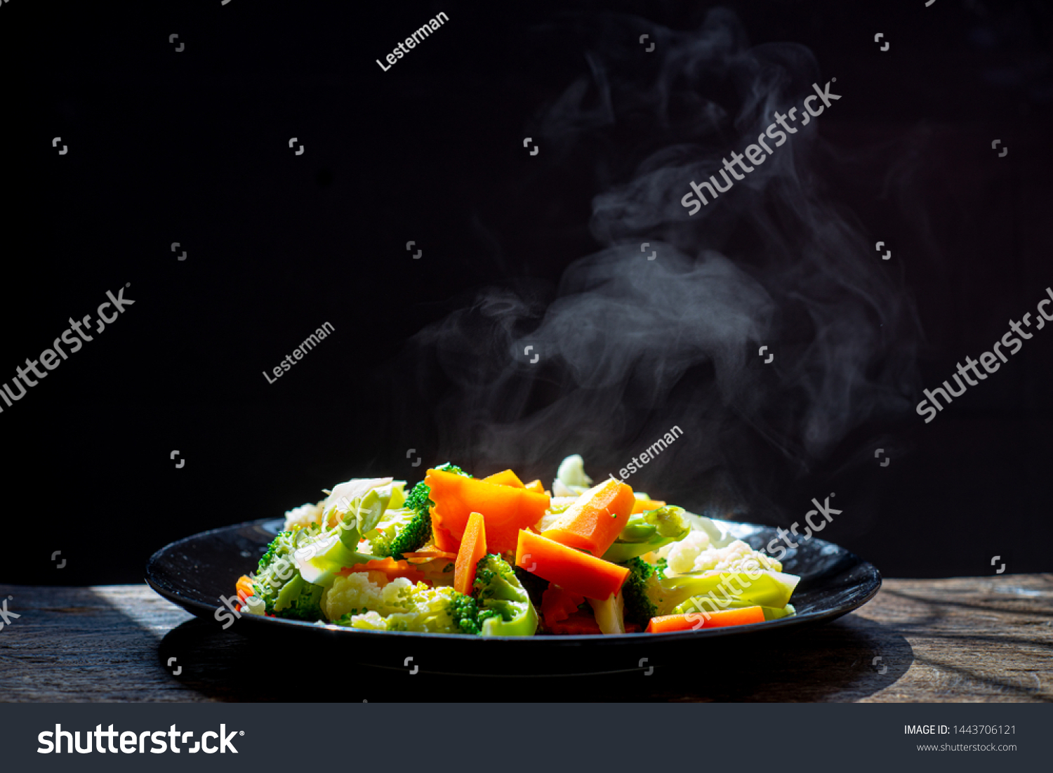 The steam from the vegetables carrot broccoli Cauliflower in a black plate  , a steaming. Boiled hot Healthy food on table on black background,hot food and healthy meal concept #1443706121