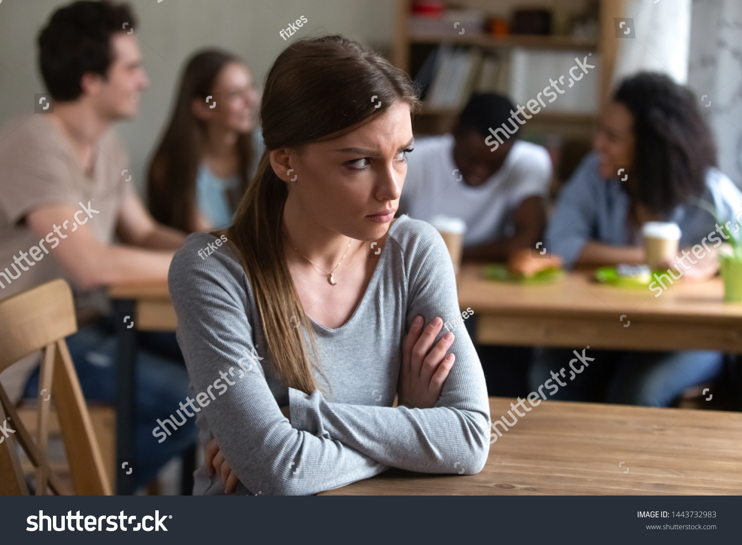 Abused upset offended by friends young caucasian woman sitting alone separately from group of happy laughing people, sad introvert feeling lonely, suffering from bullying, low self-esteem concept. #1443732983