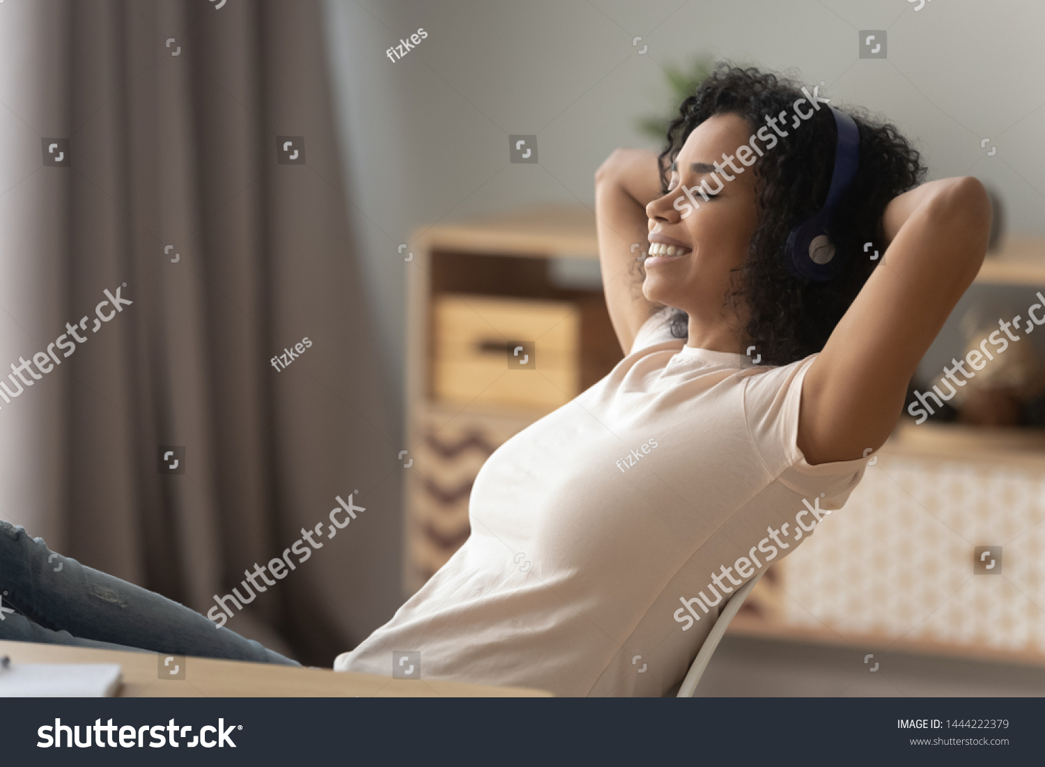 Happy african american girl wearing headphones relaxing listening to music taking break at work, calm smiling young black woman enjoying good lounge sound for stress relief sit at home office desk #1444222379