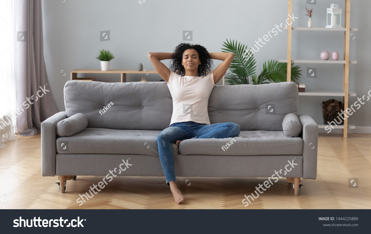 Young calm black woman relaxing sit on comfortable sofa in modern living room, lazy happy african woman girl resting on couch breathing fresh air enjoy peace of mind no stress free on couch at home #1444225889