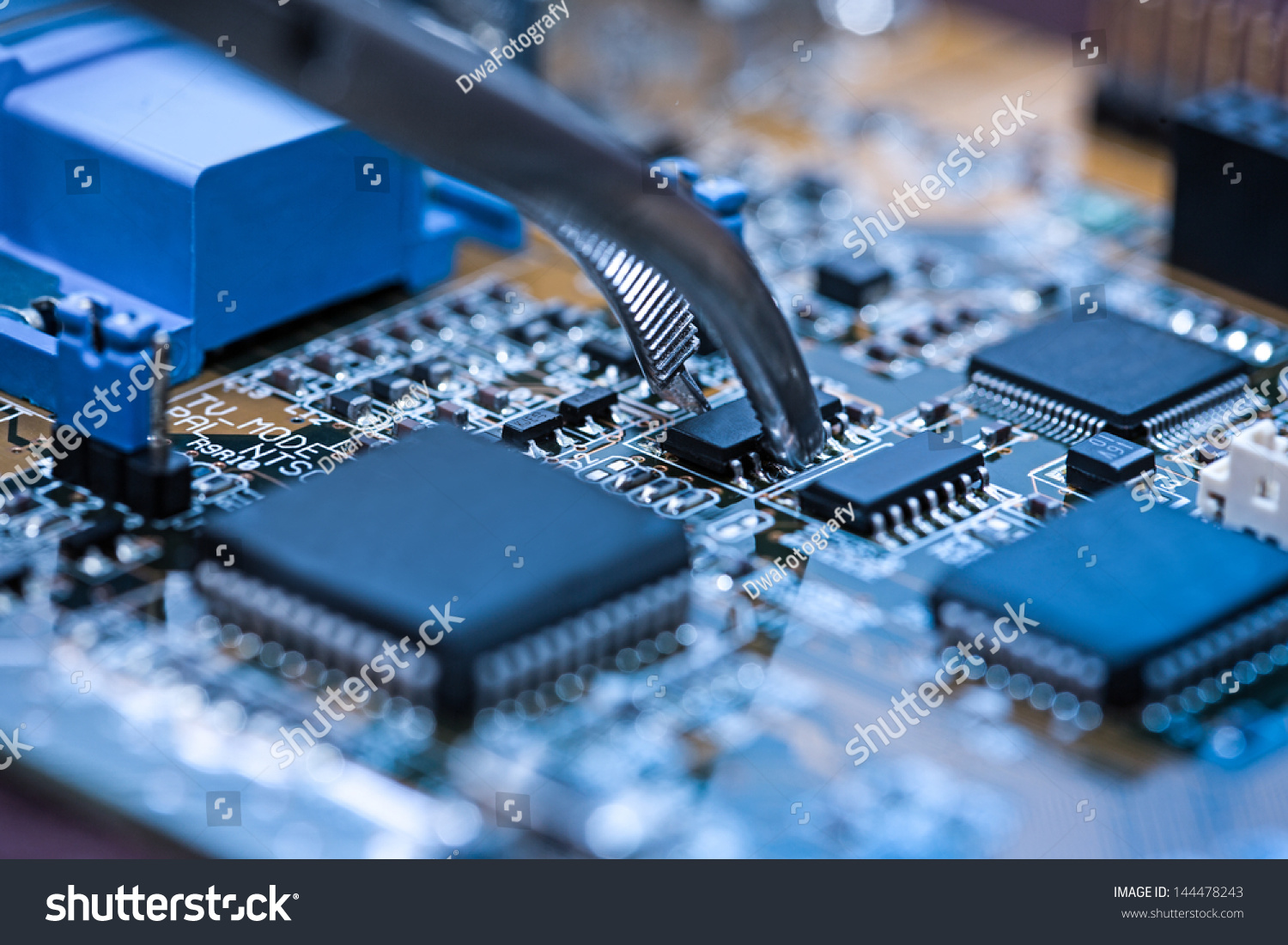 Close up on tweezers holding chip on computer circuit board. #144478243