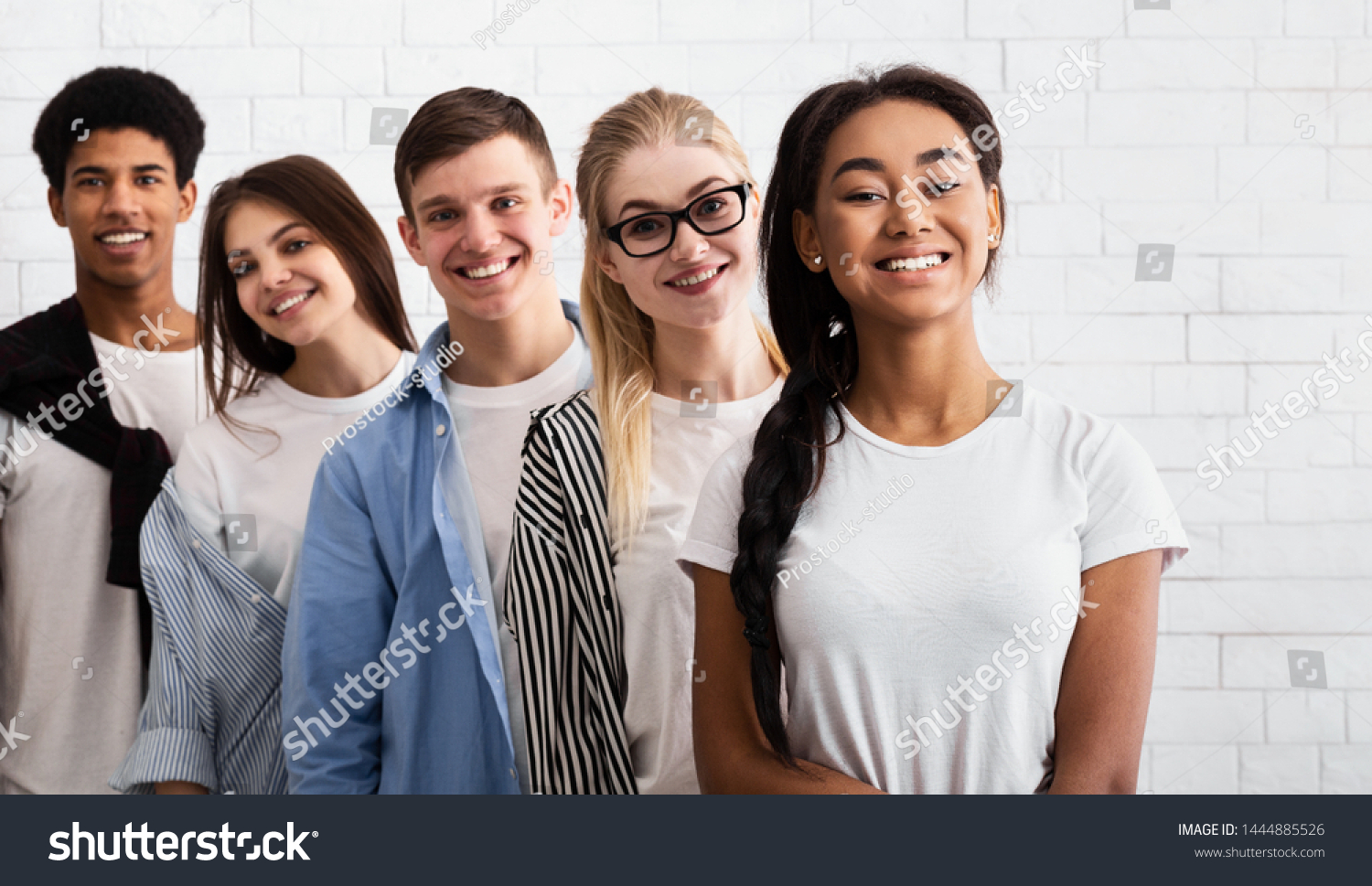 Group of teenage friends standing in line and looking at camera, white brick wall #1444885526