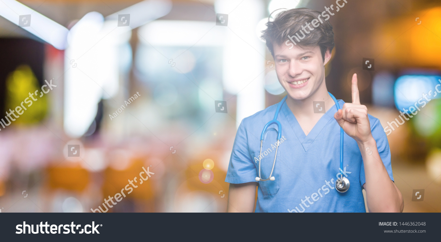 Young doctor wearing medical uniform over isolated background showing and pointing up with finger number one while smiling confident and happy. #1446362048