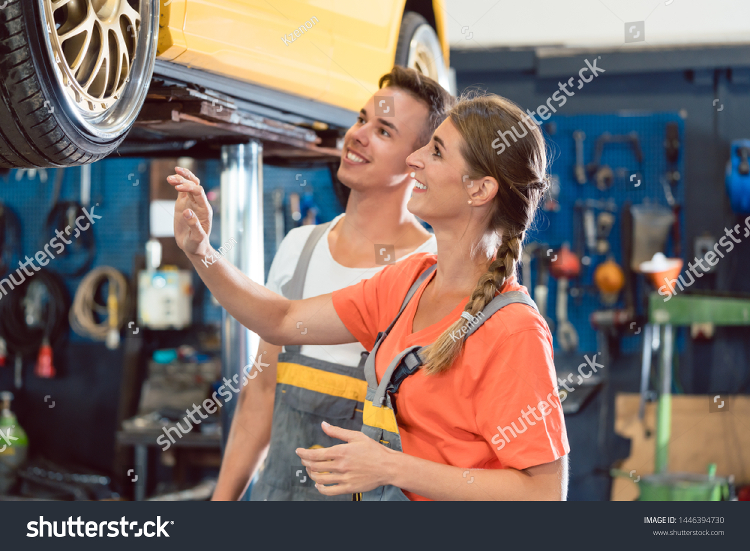 Two happy dedicated auto mechanics, checking the modified wheels of a tuned car while working together in a modern automobile repair shop with tuning service #1446394730