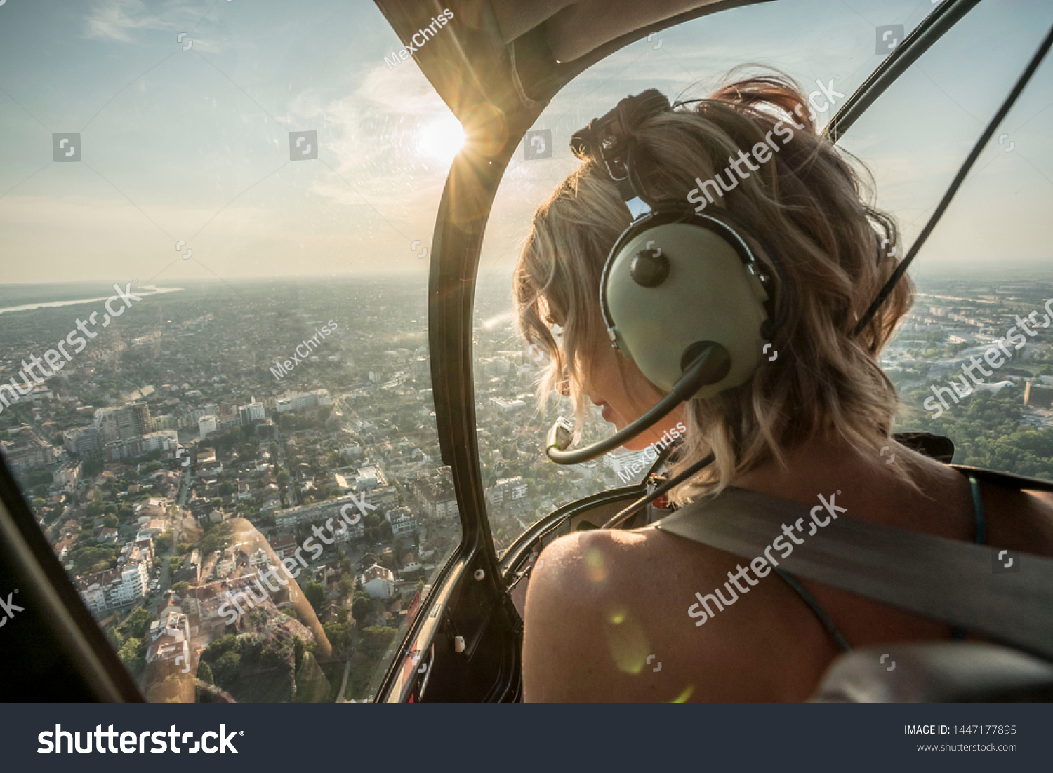 Portrait of beautiful blonde women enjoying helicopter flight. She is amazed by cityscape and wearing pilot headphones.
 #1447177895