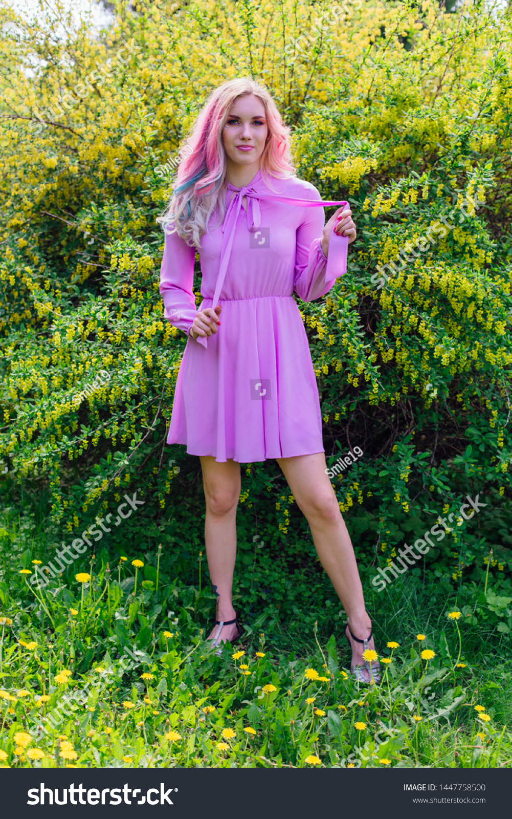 Beautiful fashion model girl with colorful dyed hair and perfect makeup and hairstyle standig next to blooming barberry bush with yellow flowers #1447758500