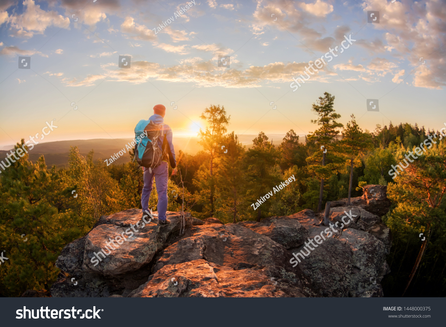 Hiker with backpack standing on a rock and enjoying sunset on mauntain #1448000375