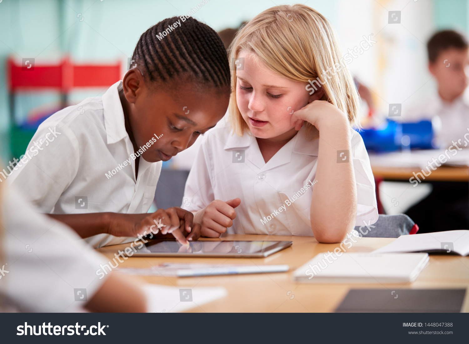 Two Elementary School Pupils Wearing Uniform Using Digital Tablet At Desk #1448047388