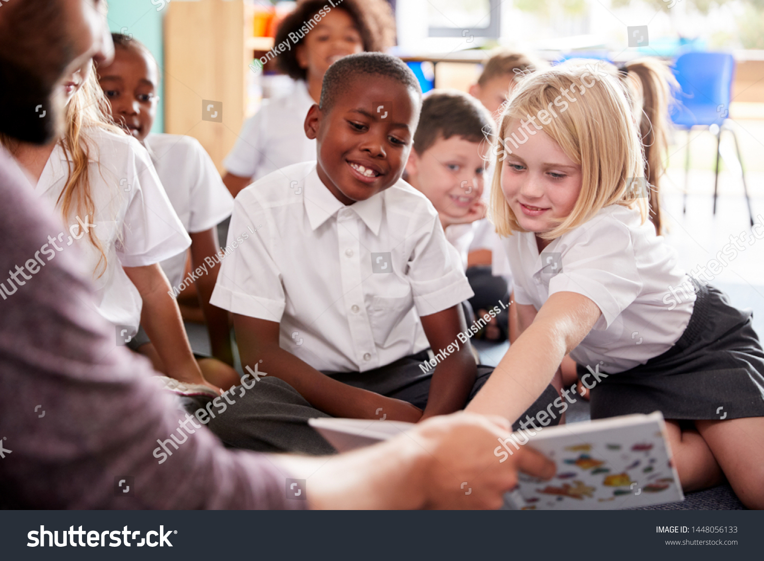 Male Teacher Reading Story To Group Of Elementary Pupils Wearing Uniform In School Classroom #1448056133