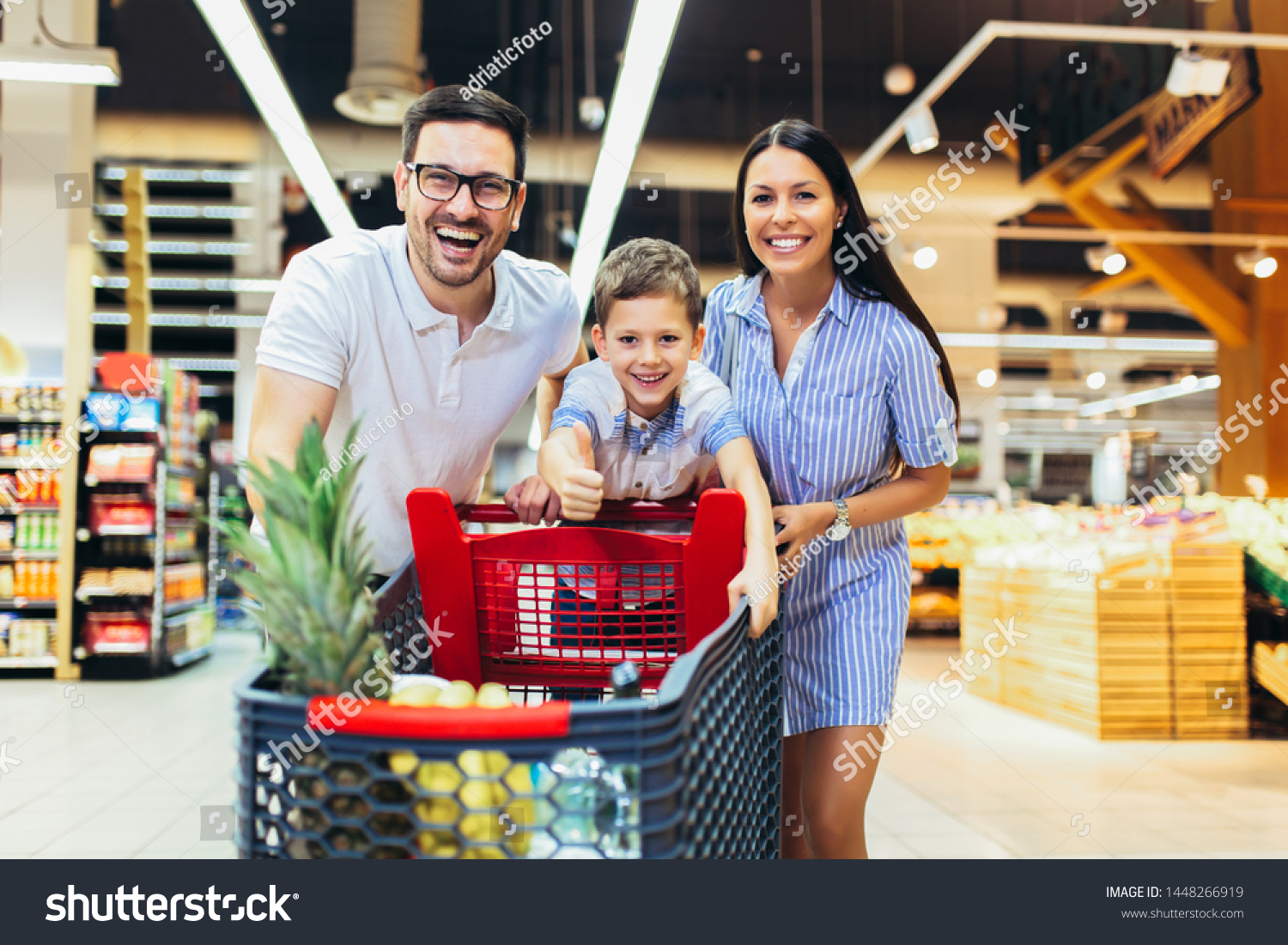 Happy family with child and shopping cart buying food at grocery store or supermarket #1448266919