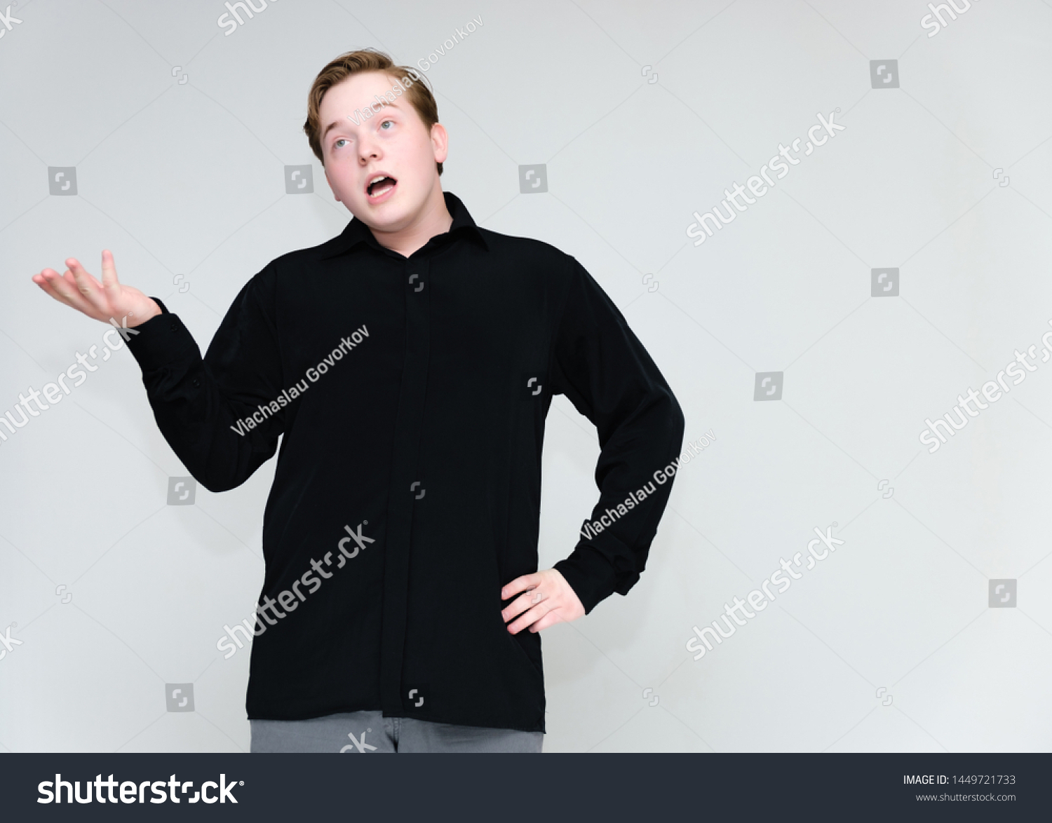 Portrait to the waist on a white background of a handsome young man in a black shirt. stands directly in front of the camera in different poses, talking, showing emotions, showing hands. #1449721733