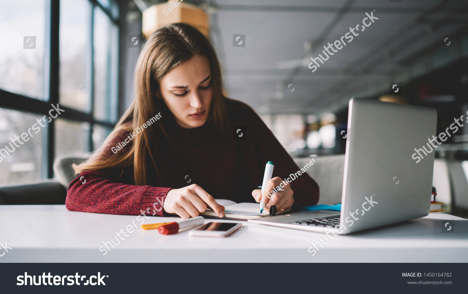 Young attractive female writer scribing notes to textbook prepare for exam, girl doing homework sitting desktop with modern laptop computer, woman making plan for tomorrow and creating  to do list #1450164782