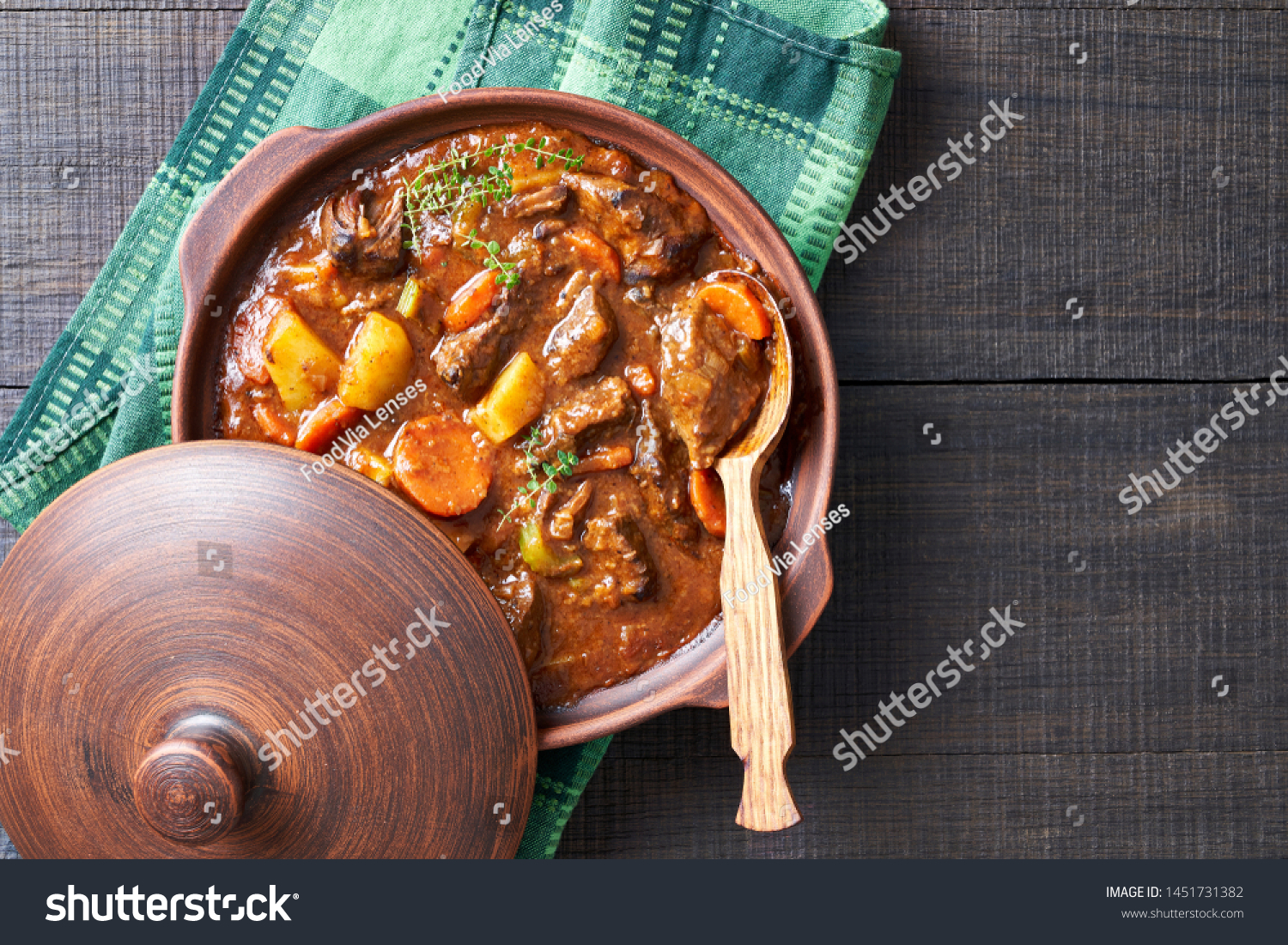 Hearty beer and lamb stew, with potato, carrot, stewed in a dark beer, with thyme stems, served in a clay pot with irish soda bread on a wooden background, top view, copy space #1451731382