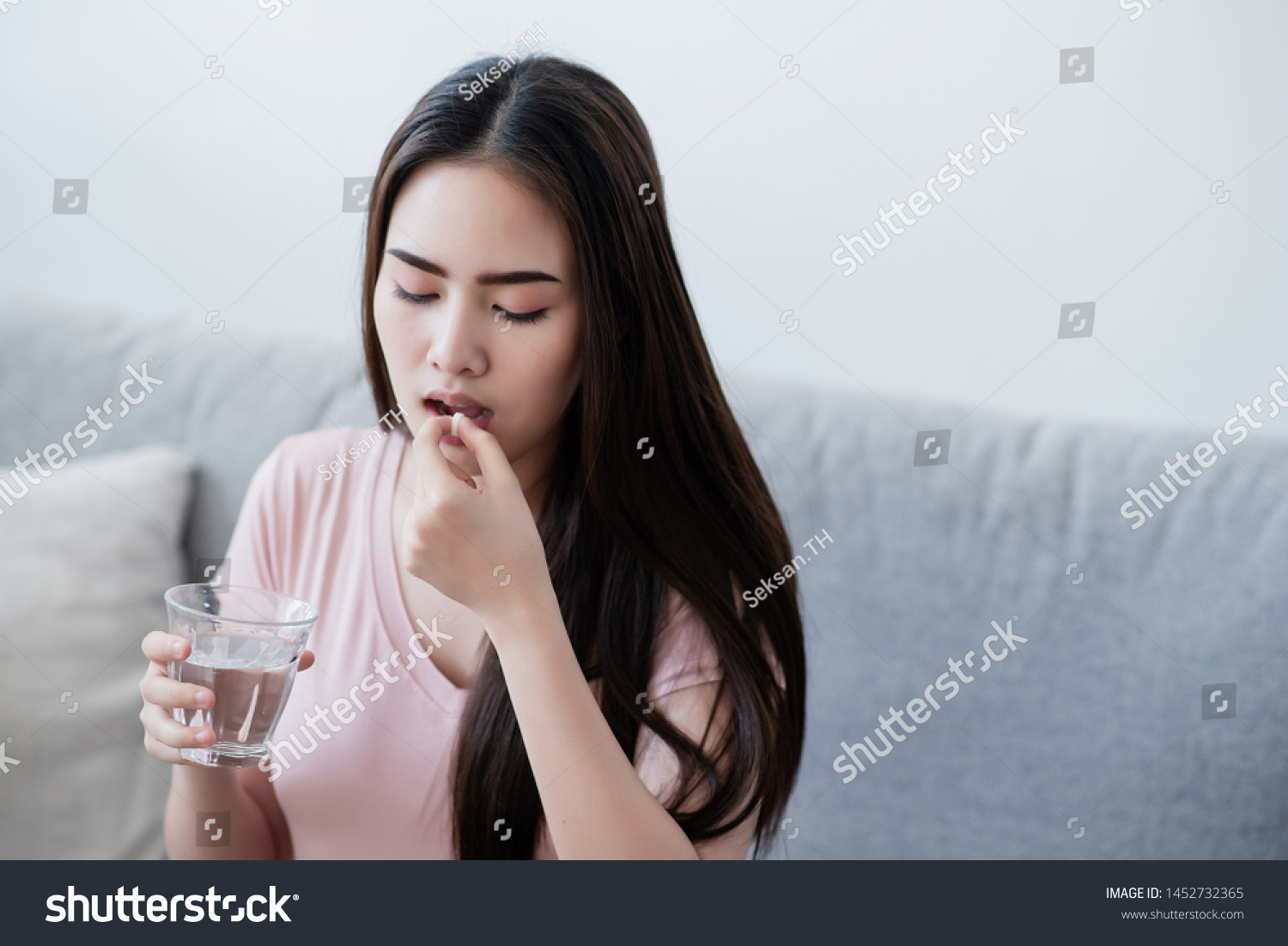 Sick woman eating pills with a glass of water in hand.
 #1452732365