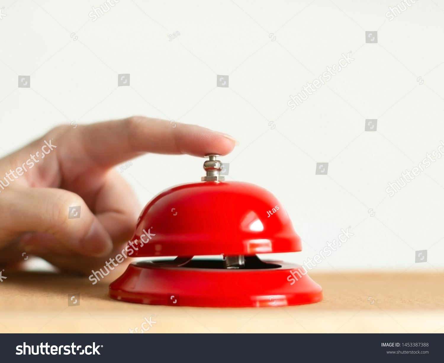 A hand press the red handbell on wooden table on white background; selected focus at the index finger that pressing the bell button. concept of calling for assistance. #1453387388