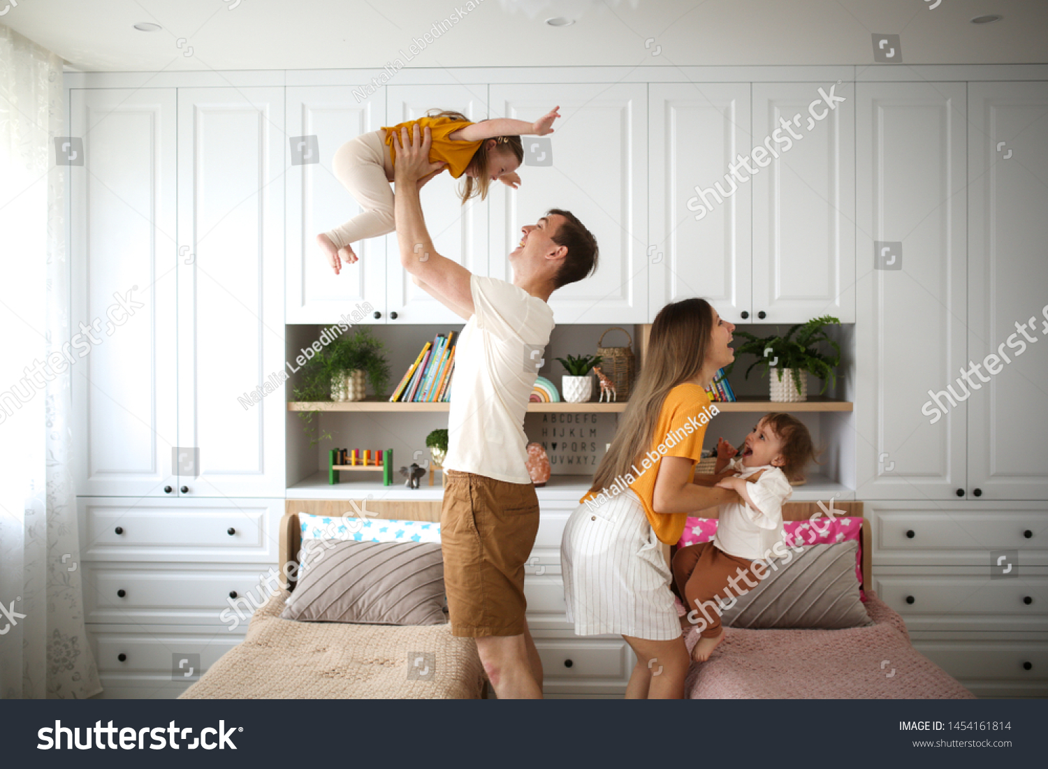 Beautiful Caucasian family with two children in their arms, dad and mom hold two children in the air, a real bright Scandinavian-style interior #1454161814