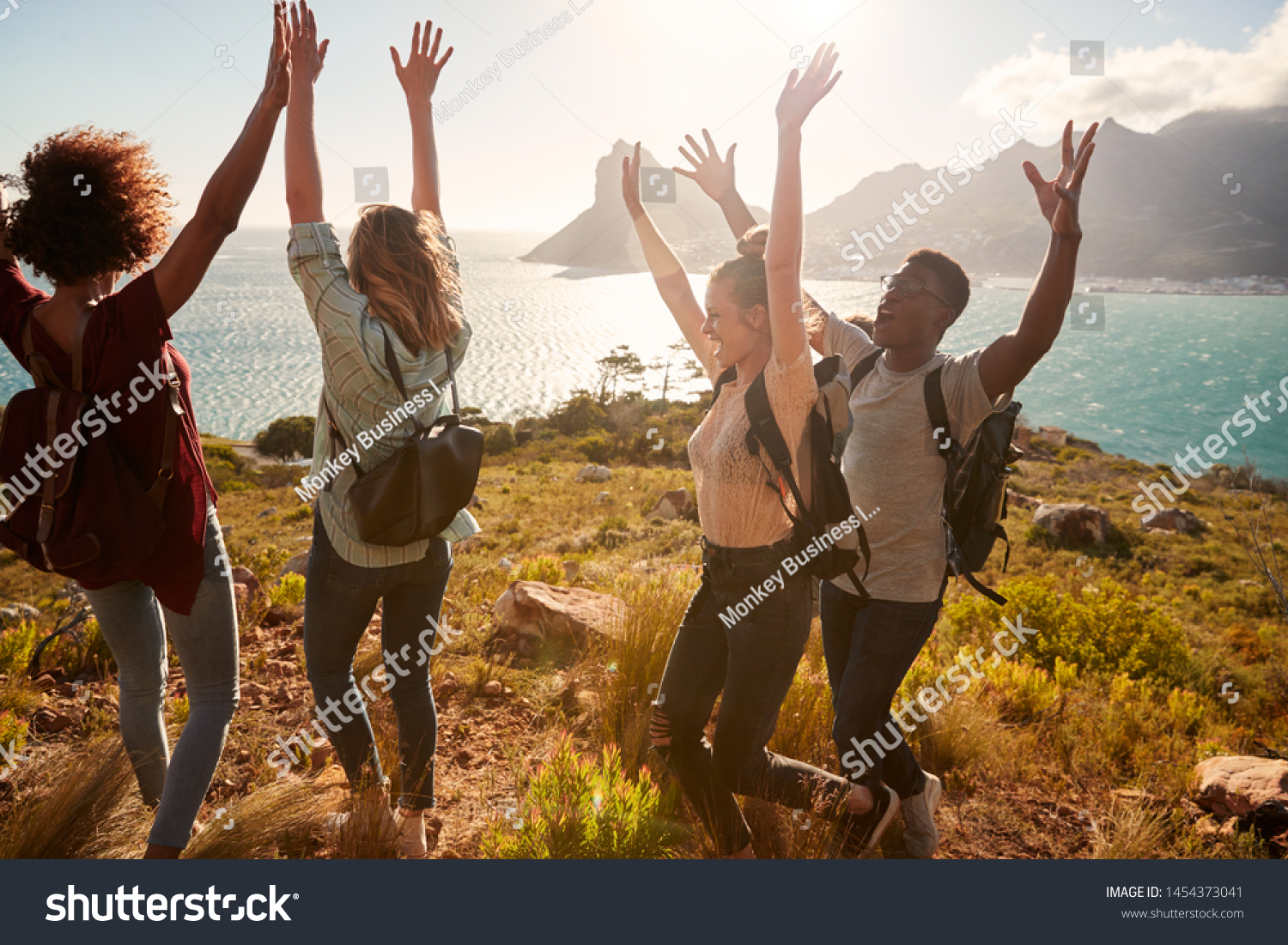 Millennial friends on a hiking trip celebrate reaching the summit, cheering with arms in the air #1454373041