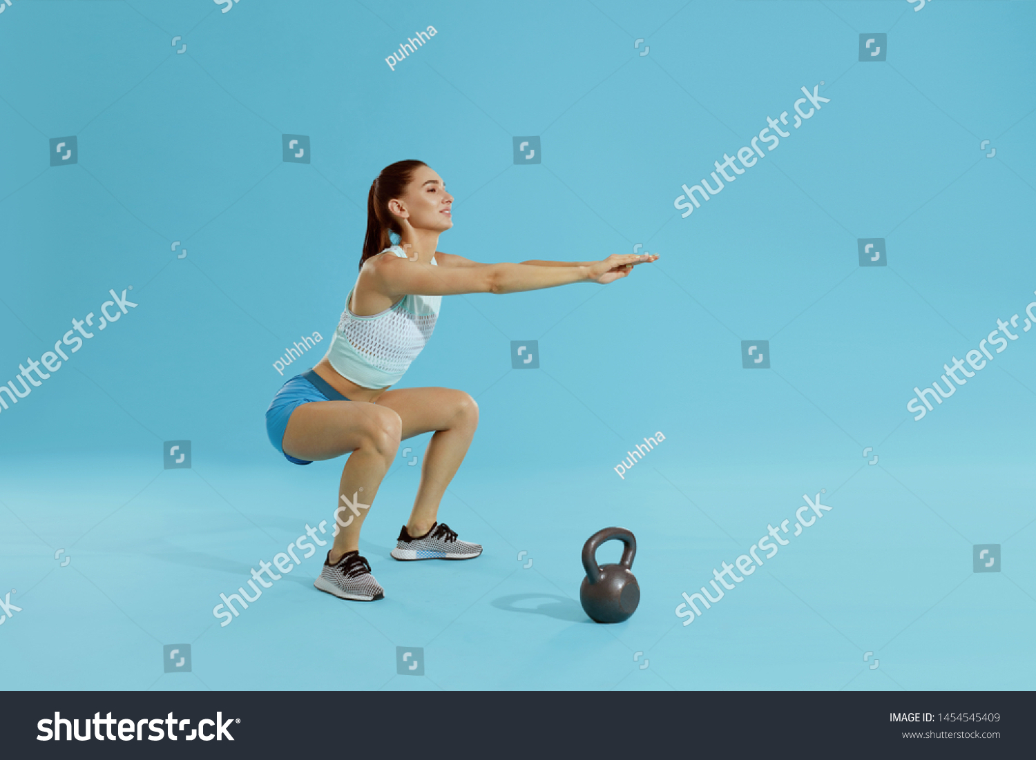 Squats. Fitness woman in sports wear exercising, doing squat workout at studio. Full length portrait of fit girl squatting on blue background #1454545409
