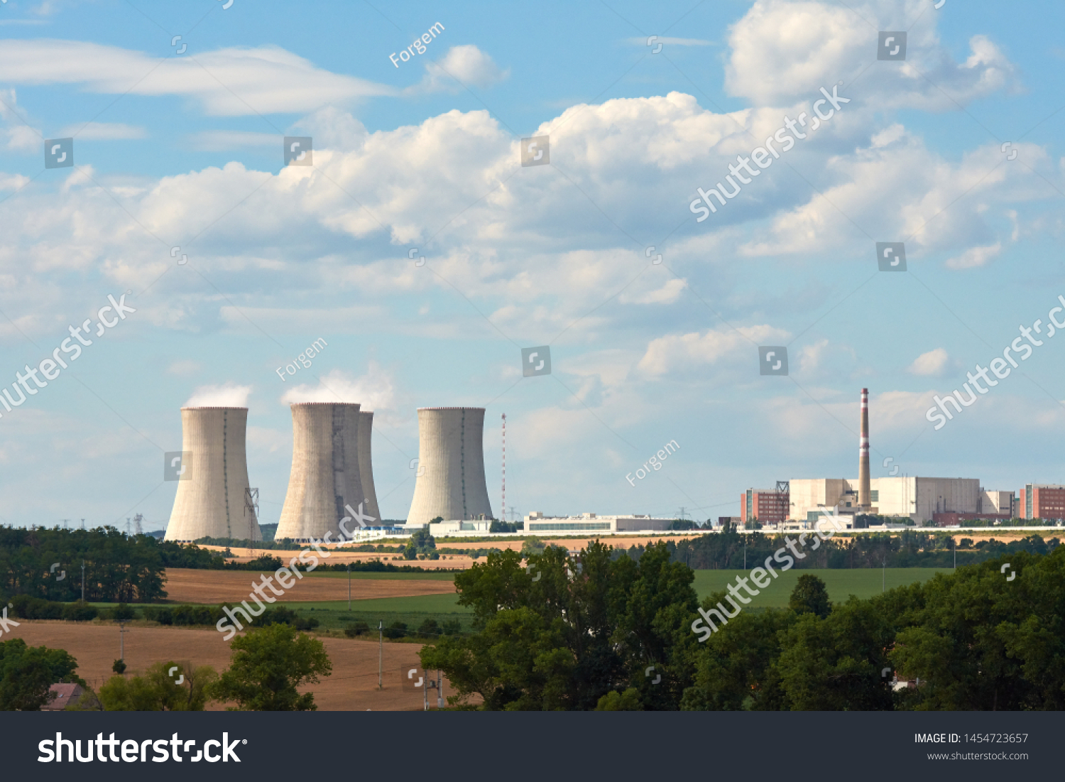 View of smoking chimneys of nuclear power plant, power lines and forest, under blue sky with white clouds #1454723657