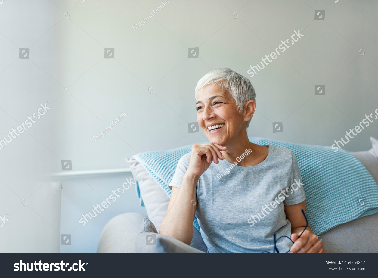 Happy woman relaxing on her couch at home in the sitting room. Portrait of beautiful mature woman smiling while sitting at sofa at home. Beautiful middle age woman smiling at home #1454763842