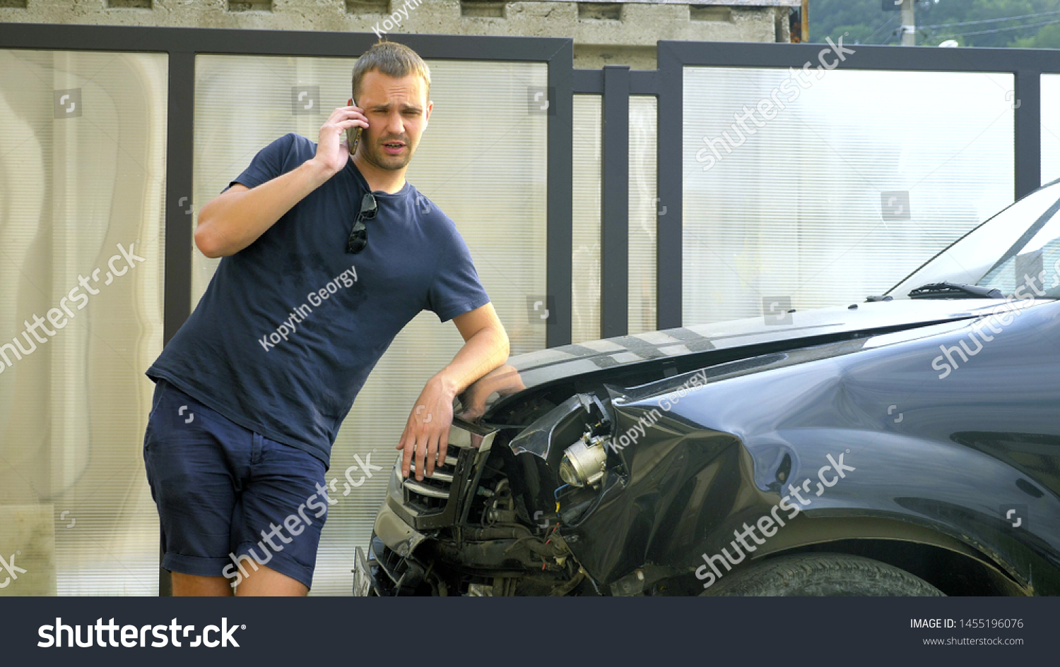 car accident concept. man in a state of shock talking on the phone after a car accident, standing by a car with a broken bumper #1455196076