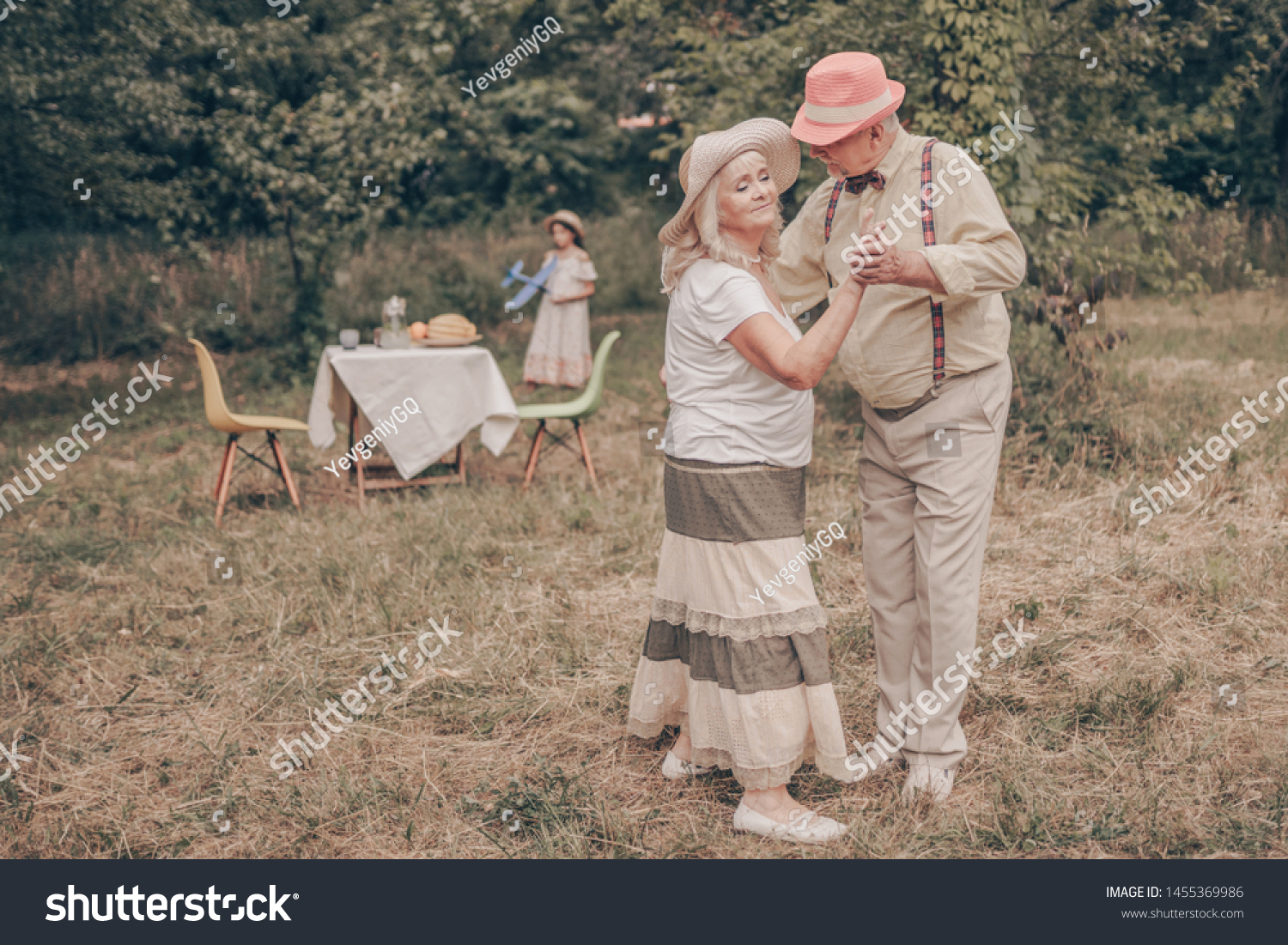 A grandfather with happy eyes looks grandmother in the eyes. Youth memories. The concept of a happy old age. Portrait of oldies who are dancing in the garden #1455369986