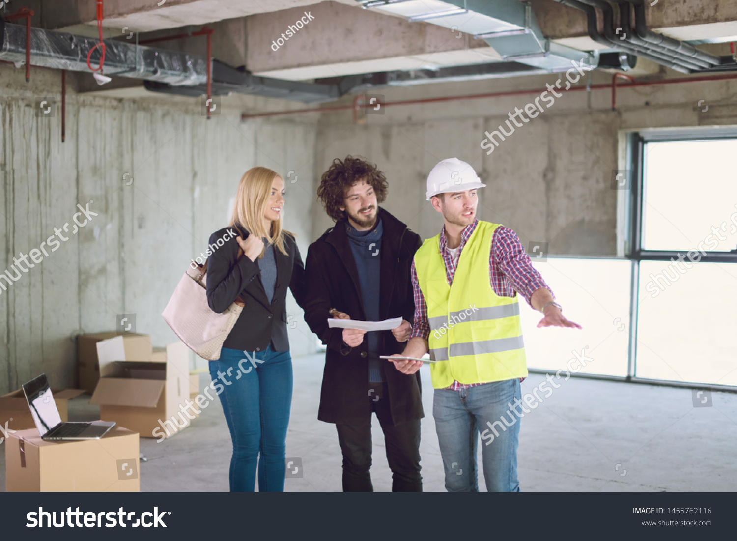 architect using tablet computer while showing house design plans to a young couple at construction site #1455762116